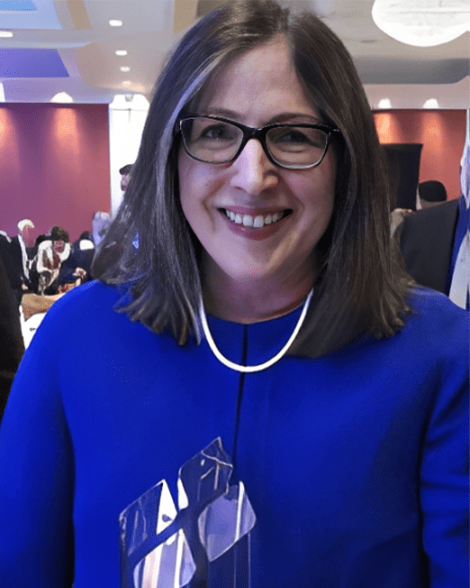 Woman in a blue outfit holding an award, smiling at an event with attendees in the background. The image highlights her achievement and celebratory atmosphere.