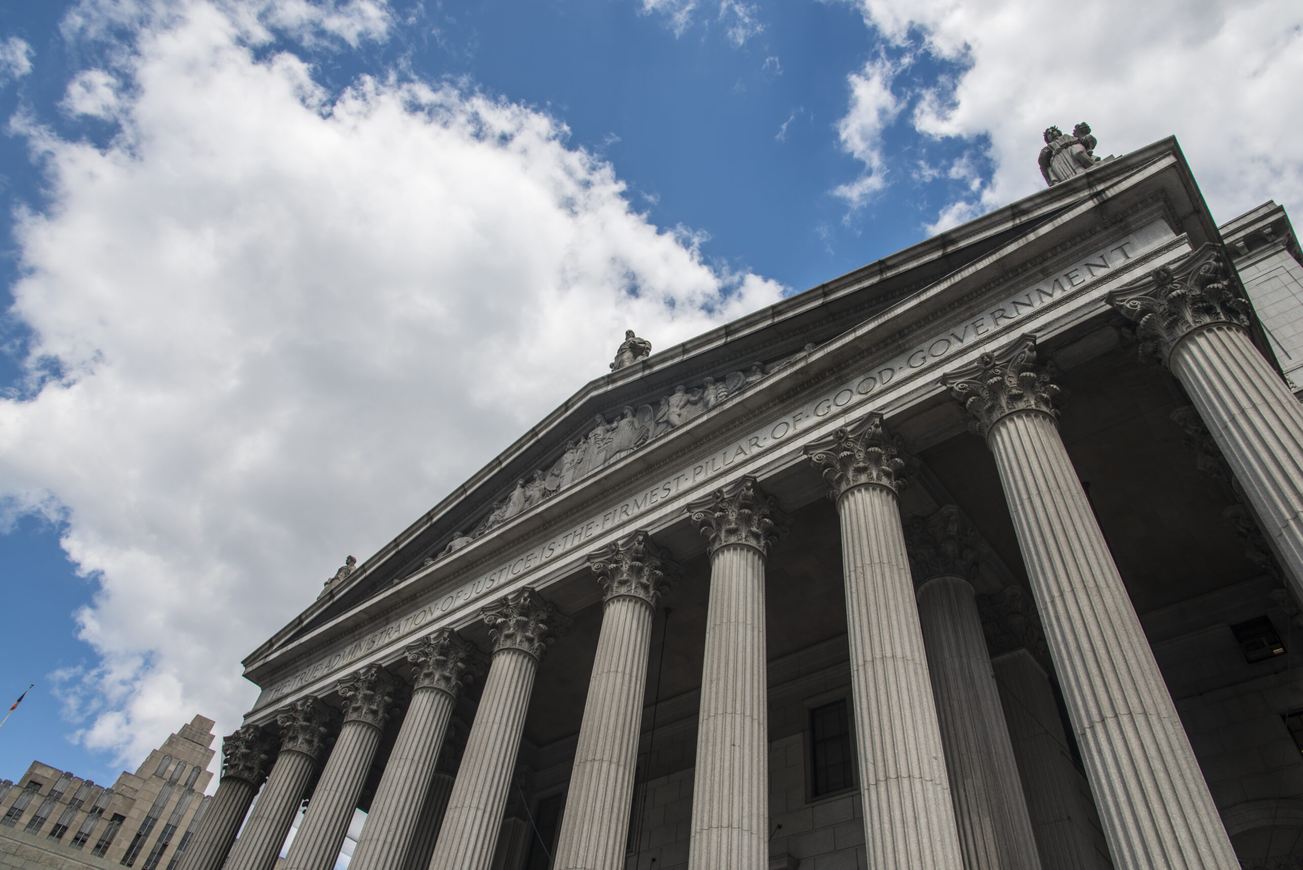 The imposing façade of a courthouse features grand columns and an inscription proclaiming, "Justice is the firmest pillar of good government."